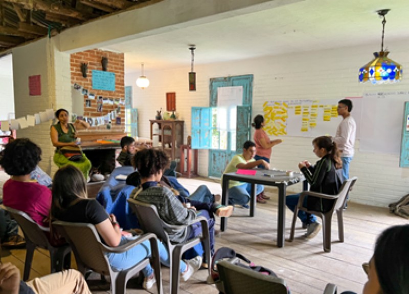 A small group of people present photos and data collected to a room of people seated. Photos can be seen hung on display across the room.